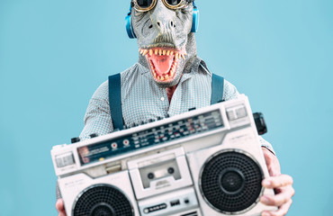 Crazy senior man wearing t-rex mask and listening to music holding vintage boombox stereo outdoor -...