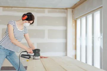 Young woman using an orbital sander on wood