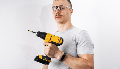 Construction: A man in protective glasses is holding a yellow electric screwdriver.