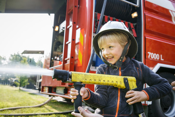 Little fireman holding firehose nozzle and splashing water.