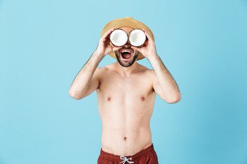 Photo of cheerful shirtless tourist man wearing straw hat smiling while holding two coconut parts