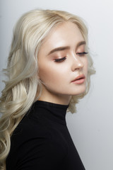 Naklejka premium Profile portrait of a woman with curly blonde hairstyle in black jumper, soft make up, model posing with closed eyes, isolated on a white background.