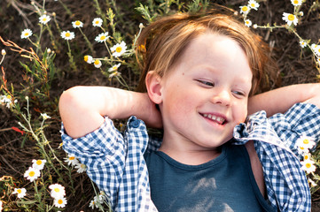 happy little boy in a plaid shirt lies in daisy field