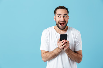 Photo of european brunette man wearing basic t-shirt laughing and holding smartphone