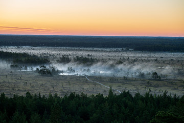 misty and cloudy sunrise above green fields and forests