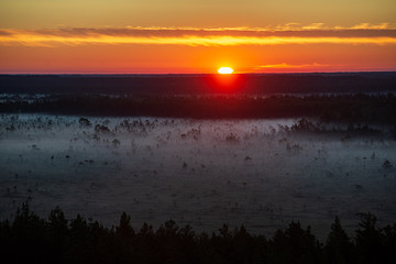 misty and cloudy sunrise above green fields and forests