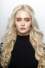 Frontal portrait of a cute blonde girl, with delicate make up, curly shiny long hair, isolated of a white background.