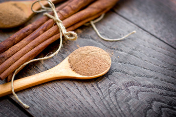 Cinnamon powder in spoon and  cinnamon sticks on rustic table