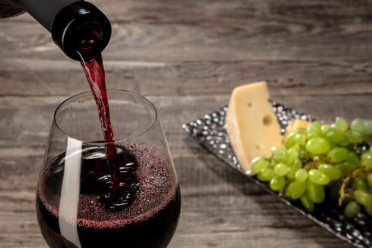 Delicisious and tasty food and drink. A bottle and a glass of red wine with fruits over weathered wooden background. Top view with copy space to insert your text or image for ad. Grape and cheeseplate