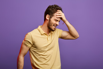 unhappy angry Caucasian man standing with closed eyes wearing stylish T-shirt , holding hand on head, looking stressful.sick man suffering from headache. health, tension, migraine concept