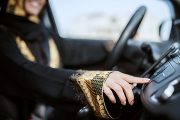 Close up of muslim woman dressed in traditional wear driving car and changing radio station.