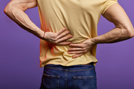 man touching his back, guy has disk peoblems in his back. close up cropped back view photo. isolated blue background