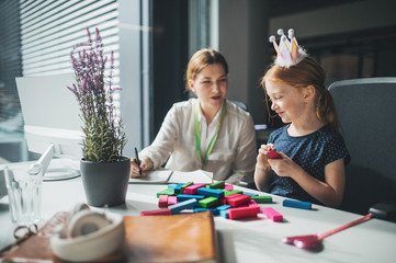 A businesswoman with small daughter sitting in an office, working and playing.