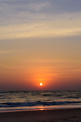 Naklejka premium Beautiful colorful sunset on the ocean, vertical photo. Sand beach, the sun sets in the clouds above the sea.