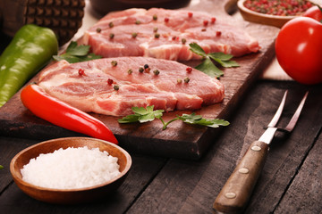 Raw meat. Raw pork steak on a cutting board with vegetables, peppers, tomato, salt and spices on a black background