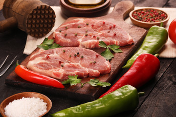 Raw meat. Raw pork steak on a cutting board with vegetables, peppers, tomato, salt and spices on a black background