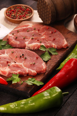 Raw meat. Raw pork steak on a cutting board with vegetables, peppers, tomato, salt and spices on a black background