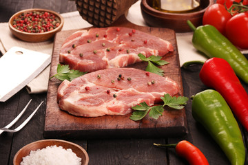 Raw meat. Raw pork steak on a cutting board with vegetables, peppers, tomato, salt and spices on a black background