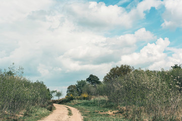 Dirt road uphill in cloudy countryside.