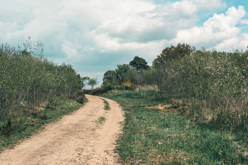 Dirt road uphill in cloudy countryside.