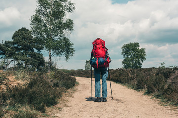 Backpacker going uphill on dirt road under blue cloudy sky.