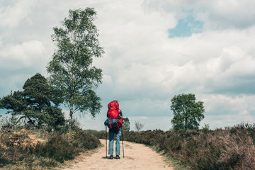 Backpacker going uphill on dirt road under blue cloudy sky.