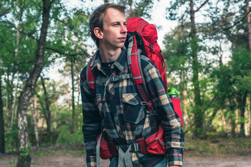 Young man with red backpack in forest in spring.