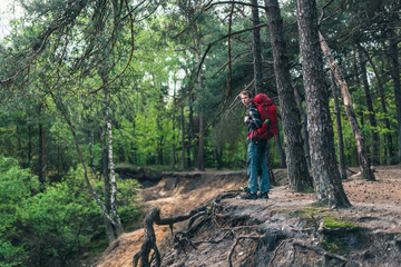 Obraz premium Young man with red backpack at edge of canyon in spring forest.