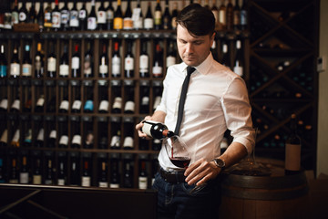 pleasant man holding a bottle of good wine and glass and posing to the camera at workplace. lifestyle concept