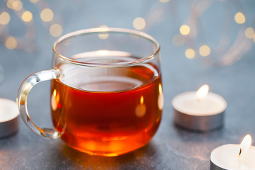 Black tea in glass cup with candles and light garland. Grey background. Copy space.