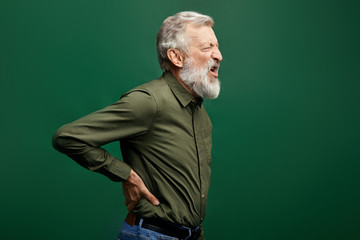angry shouting old man suffering from back pain isolated on green background. close up side view...