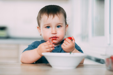A little girl in the kitchen eating ripe strawberries very appetizing and tasty