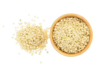 Wooden bowl with peeled or shelled hemp seeds and a pile next to seen directly from above and isolated on white background