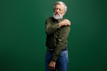 sick old man has pain in neck, senior man has shoulder dislocation. weak man suffering from strong pain. close up photo. isolated green background