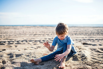 Fototapeta na wymiar A small girl playing in sand outdoors on beach.