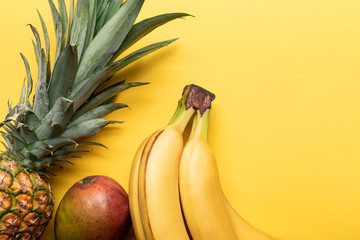 top view of whole ripe bananas, pineapple and mango on yellow background