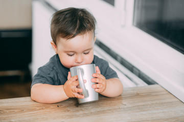 A little girl in the kitchen drinking water from a silver mug very greedily