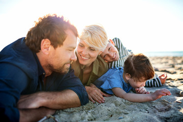 Young family with two small children lying down outdoors on beach.