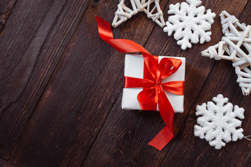 Christmas greetings card. White gift box with red ribbon and snowflakes on a wooden background with place for your text