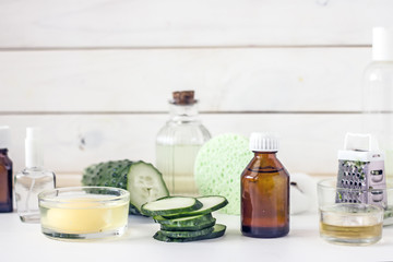 Bottle with homemade cucumber lotion, fresh plastics of cucumbers, yolk and other skin care ingredients. Set of bottles and bowls with organic skin care cosmetics on a table against a wooden wall. Nat