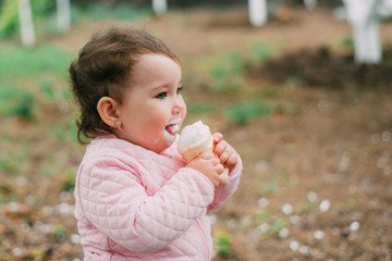 little girl in the garden on the background of greenery and trees very cute eating ice cream in a waffle Cup