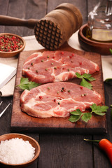 Raw meat. Raw pork steak on a cutting board with vegetables, peppers, tomato, salt and spices on a black background