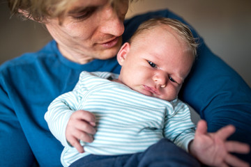 A front view of young father holding a newborn baby at home.