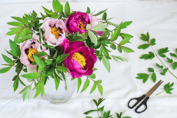 Pink and purple peonies in a vase on a white table, view from above
