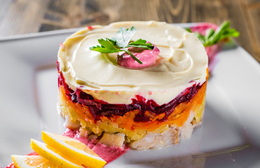layered salad with herring, beets, carrots, onions, potatoes and eggs close-up on a plate on wwoden table