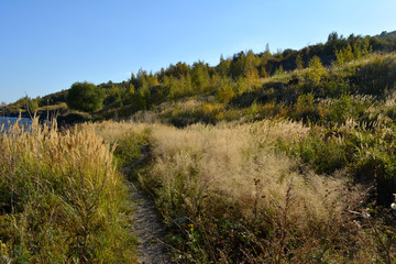 Fototapeta na wymiar Path through meadow with dry herbs to the hills on river bank. Nature in the beginning of autumn.