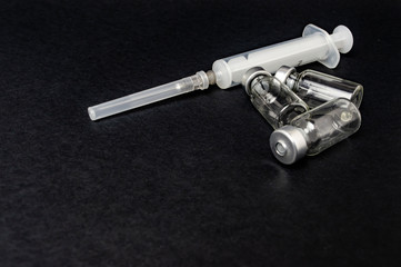 Glass vials of vaccines and syringe on black background closeup