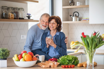 A portrait of senior couple in love indoors at home, holding coffee.