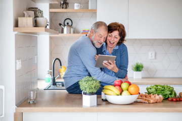 A portrait of senior couple in love indoors at home, using tablet.