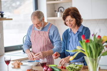 A portrait of senior couple in love indoors at home, cooking.